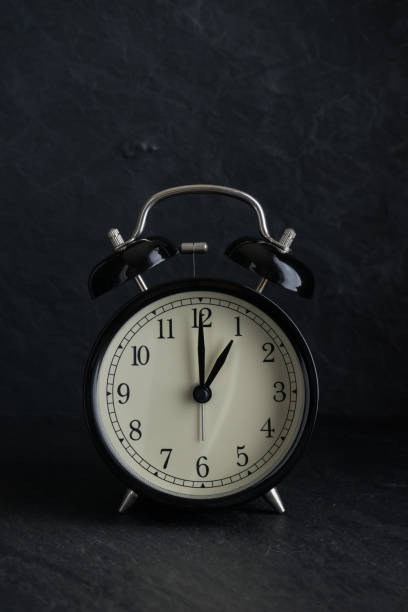 istock black alarm clock with stone background at one o'clock 842836182