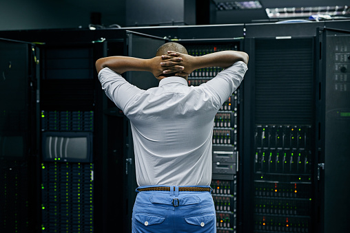Rearview shot of an IT technician having difficulty repairing a computer in a data center