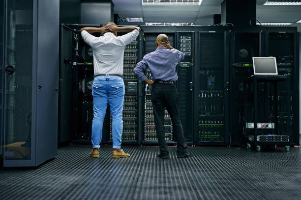 Meanwhile in the server room... Rearview shot of two IT technicians having difficulty repairing a computer in a data center backup stock pictures, royalty-free photos & images