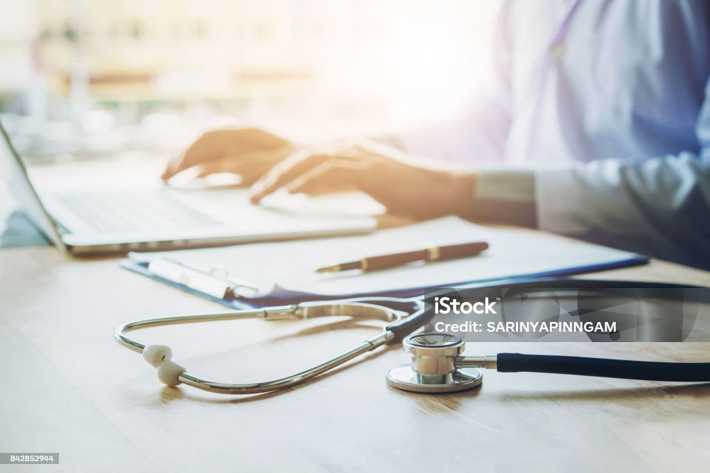 Doctor typing information on Laptop in Hospital office focus on Stethoscope Healthcare And Medicine Stock Photo