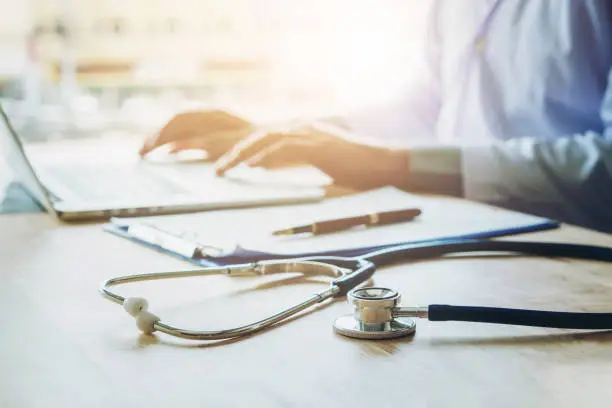 Photo of Doctor typing information on Laptop in Hospital office focus on Stethoscope