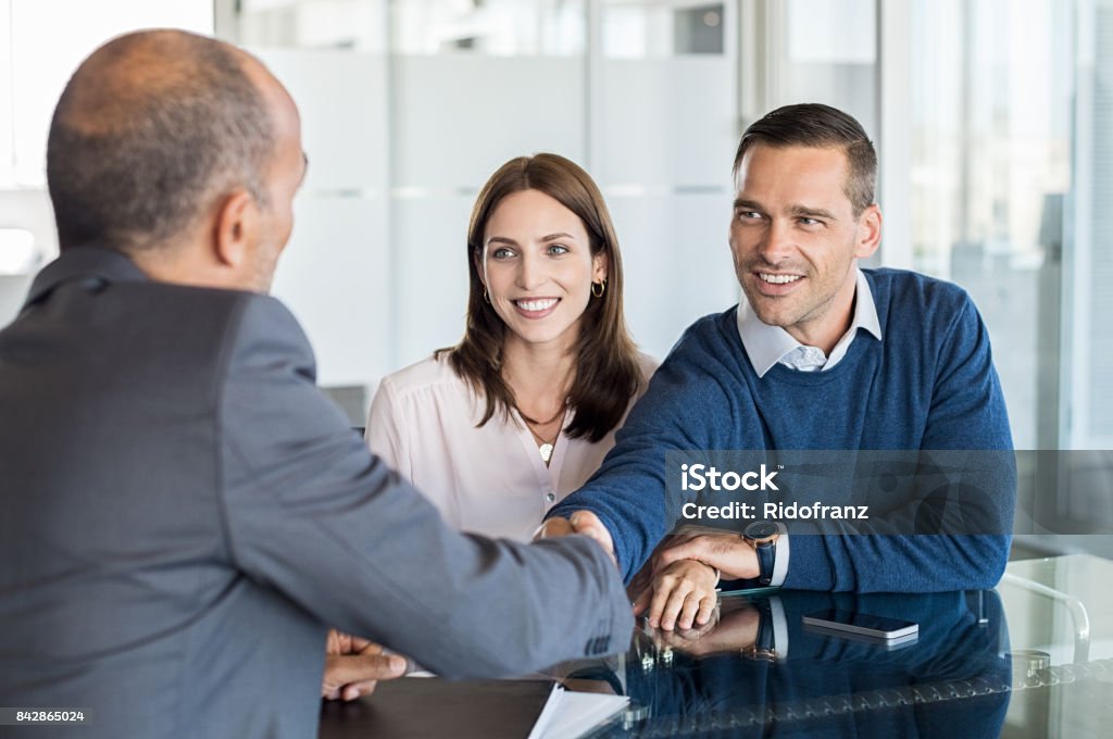 Couple meeting with financial advisor Businessman shaking hand with a young couple in office. Bank agent and his client shaking hands in conference room. Happy smiling couple seal a deal with their personal financial advisor. Handshake Stock Photo