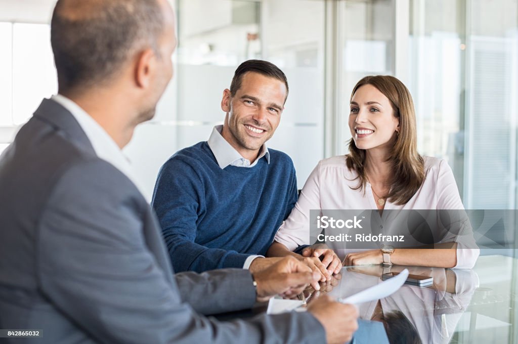 Businessman with customers Mature financial advisor showing report to young couple for their investment. Salesman and positive couple talking about purchase. Happy couple consulting financial agent for loan. Financial Advisor Stock Photo
