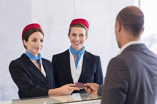 Woman in checkin counter taking passport for verification from passenger man. Happy smiling hostess at check in working with her colleague. Businessman on a business trip in airport.