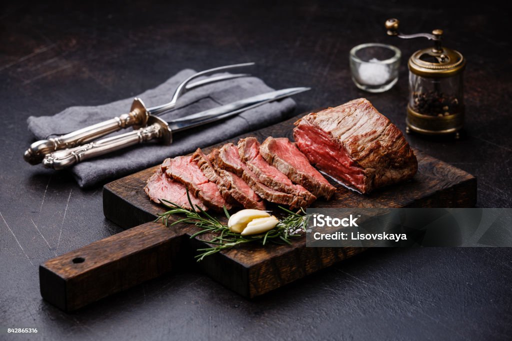 Sliced Tenderloin meat Roast beef and carving set Sliced Tenderloin meat Roast beef on cutting board with knife and fork carving set, saltcellar and pepper mill Beef Stock Photo