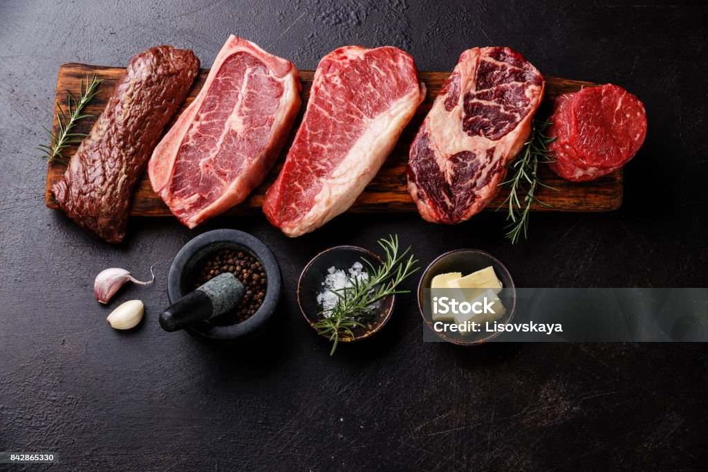 Variety of Raw Black Angus Prime meat steaks and seasoning Variety of Raw Black Angus Prime meat steaks Machete, Blade on bone, Striploin, Rib eye, Tenderloin fillet mignon on wooden board and seasoning Steak Stock Photo