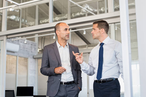 Businessmen discussing work Two businessmen discussing project at meeting at office. Business executive man and colleague standing in modern office hallway discussing project. Young businessman and mature leader talking at office. men standing business formalwear stock pictures, royalty-free photos & images