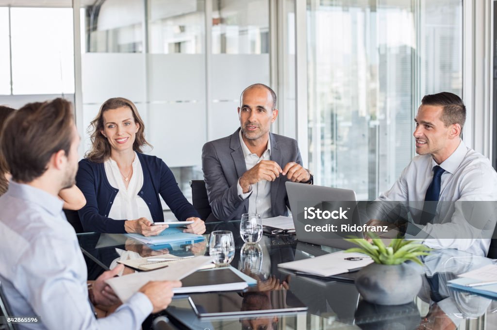 Business meeting Multiethnic group of business people sitting in annual meeting in conference room. Mature leader with businessmen and businesswomen discussing. Busy partners working together in modern office. Business Meeting Stock Photo