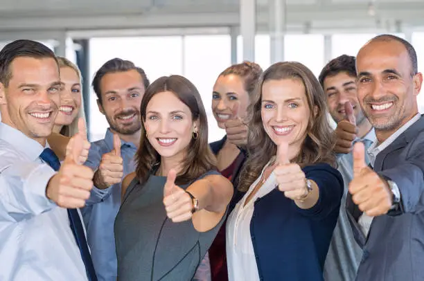 Group of happy business people showing sign of success. Successful business team showing thumbs up sign and looking at camera. Smiling businessmen and businesswomen cheering at office.