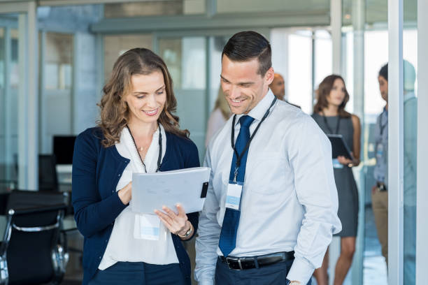 Business people at meeting Company employees reading report file at business annual meeting. Manager and smiling businesswoman working together in modern office. Happy businessman and business woman discussing report outside conference room. badge photos stock pictures, royalty-free photos & images