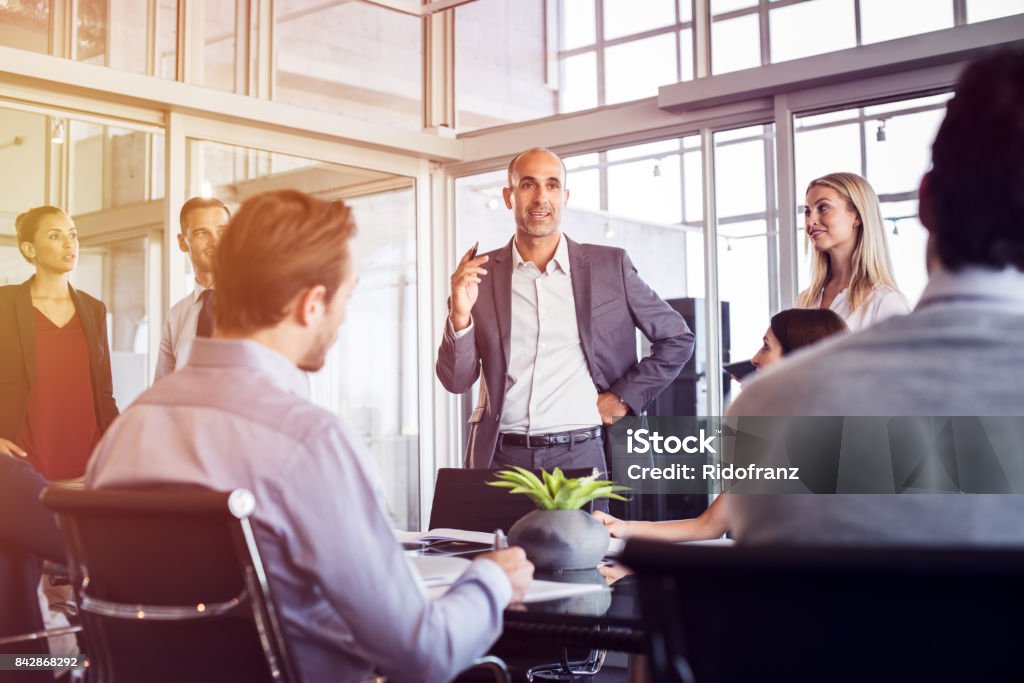 Businessman talking in meeting Senior man talking to employees in office meeting. Marketing team discussing new ideas with manager during a conference. Senior leadership training future businessmen and businesswomen. Leadership Stock Photo