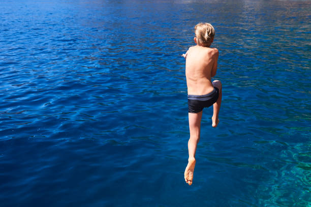 istock The child boy is jumping into the blue sea 842873076