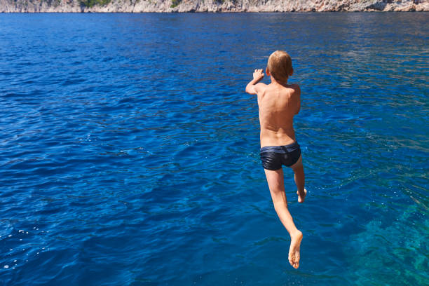 istock The child boy is jumping into the blue sea 842873200