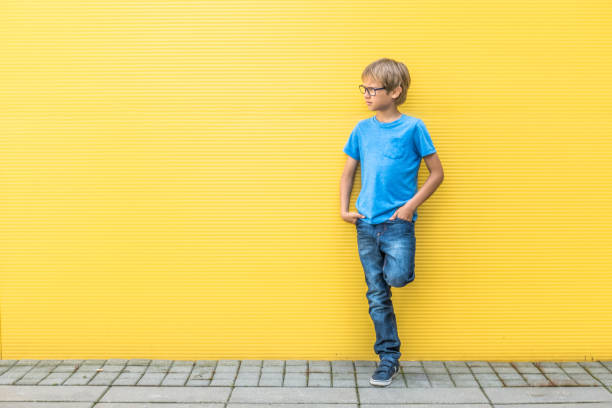 istock Boy with glasses standing near yellow wall oudoors 842883122