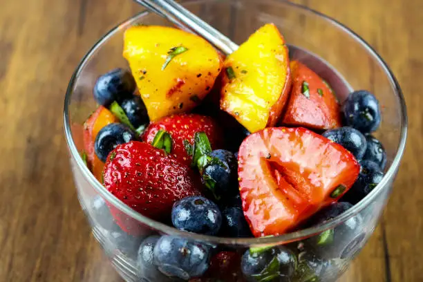 A bowl of fresh strawberries, blueberries and peaches with fresh mint