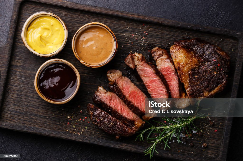 Sliced Rib eye steak and three different sauces Sliced grilled Rib eye steak and three different sauces: Pepper sauce, Mustard and Barbecue on dark background close up Steak Stock Photo