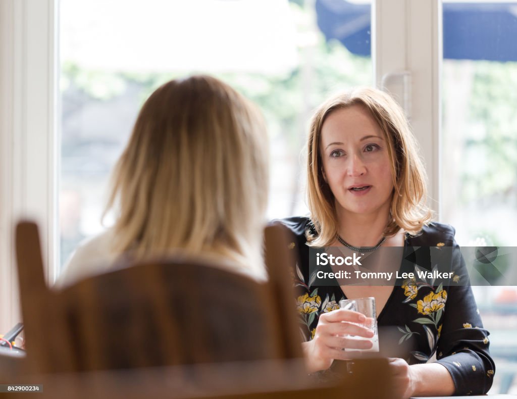 Two young adult women having friends chat in pub Young adult woman listen to opponent at informal business meeting. Horizontal low angle perspective, candid shot. Discussion Stock Photo