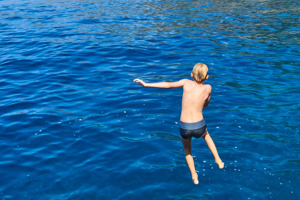 istock The child boy is jumping into the blue sea 842903110