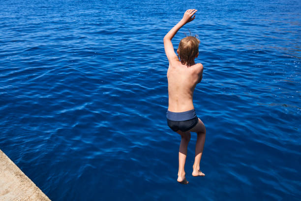 istock The child boy is jumping into the blue sea 842903696