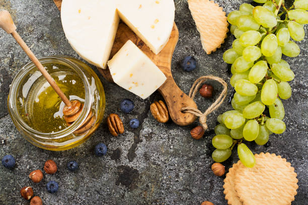 Young white cheese, a new recipe for cheese with fenugreek, a hard chopped Parmesan on a gray stone background with blueberries, nuts, green grapes, honey. Top view. Selective focus..