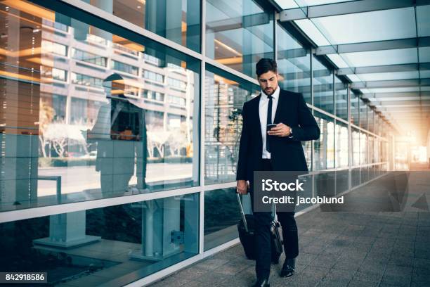 Businessman Walking With Luggage And Using Mobile Phone At Airport Stock Photo - Download Image Now