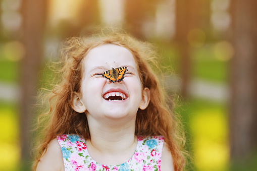 Chica rizada ríe divertida con una mariposa en la nariz. photo