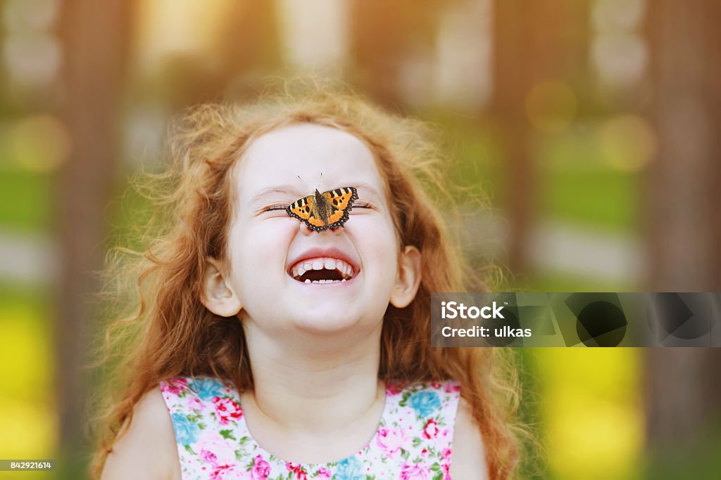 Chica rizada ríe divertida con una mariposa en la nariz. - Foto de stock de Niño libre de derechos