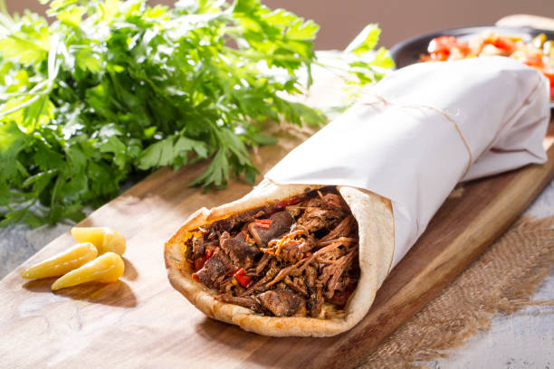 Shawarma ; Grilled Lamb Kebab Doner Wrap with yogurt, pickel, onion, aubergine and tomato on rustic white painted rustic wood table. stock photo