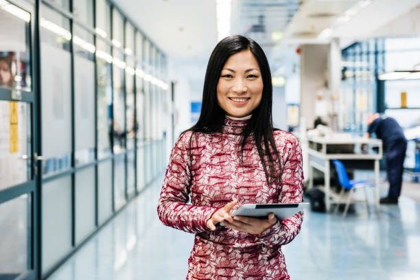 Asian Engineer With Digital Tablet In Factory Female asian engineer standing in a huge factory hallway with digital tablet asian female engineer stock pictures, royalty-free photos & images
