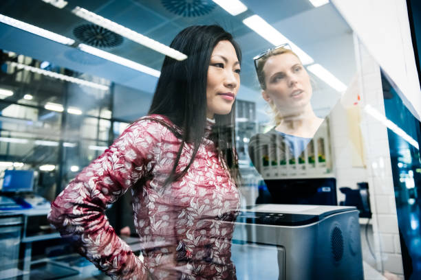 Female Engineers Discussing Two female engineers discussing a project in an industrial office while looking at documents pinned on a glass wall asian female engineer stock pictures, royalty-free photos & images