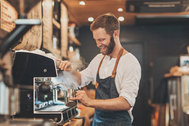Male barista making cappuccino Smiling male barista preparing cappuccino in a coffee shop making stock pictures, royalty-free photos & images