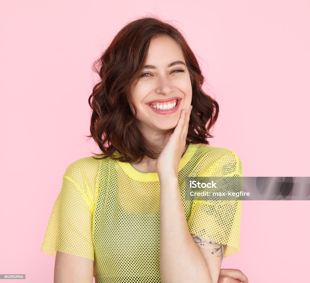 Brunette woman in yellow shirt smiling Young brunette woman wearing sheer yellow t-shirt smiling touching cheek with hand. Women Stock Photo