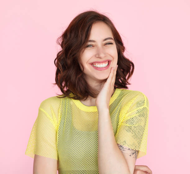 Brunette woman in yellow shirt smiling Young brunette woman wearing sheer yellow t-shirt smiling touching cheek with hand. wavy hair stock pictures, royalty-free photos & images