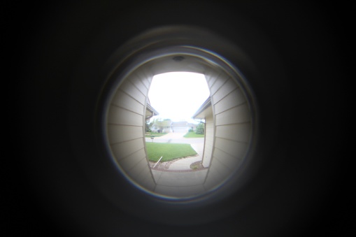 The lens of a camera is looking through a door's peephole and sees a whole world on the other side.