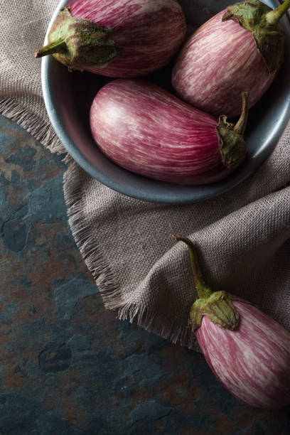 istock Colored eggplant in a tin bowl on a linen napkin on a blue stone 842965170