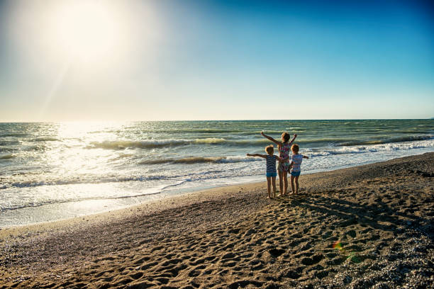 Brothers and sister are enjoying sunset at tuscany beach near Bibbona. Kids are cheering and looking at the sea.