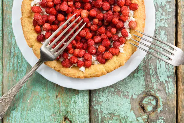 Forest strawberry and cottage cheese tart with vintage melchior forks on old turquoise table overhead view