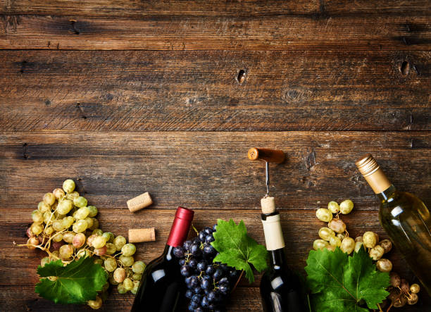 istock Wine bottles with grapes on wooden rustic background with copy space. Red and white wine. Top view. 842977388