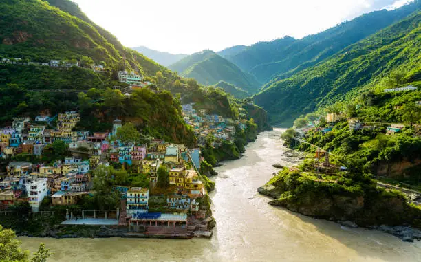 Confluence of two rivers Alaknanda and Bhagirathi give rise to the holy river of Ganga / Ganges at one of the five Prayags called Dev Prayag. Lush greenery in monsoons on the mountains. sunrise. India