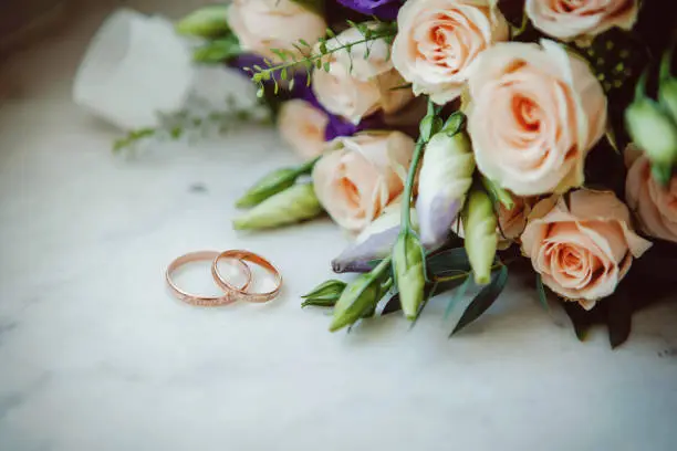 Beautiful wedding rings lie on a table against the background of a bouquet of flowers