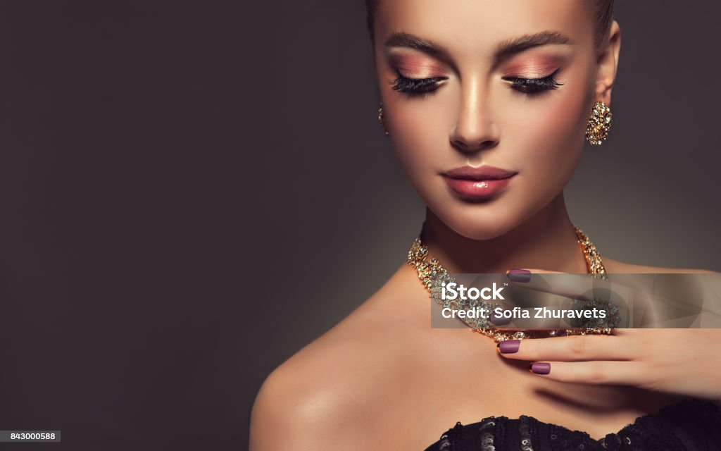 Magnificent lady in a perfect make up is shows jewelry set. Beauty portrait of young gorgeous woman is dressed in a jewelry set of necklace, ring and earings. Pretty  blue eyed model is demonstrating an attractive make up and manicure. Jewelry Stock Photo