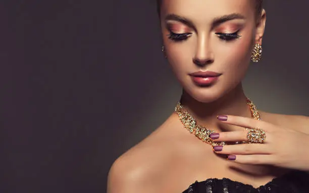 Beauty portrait of young gorgeous woman is dressed in a jewelry set of necklace, ring and earings. Pretty  blue eyed model is demonstrating an attractive make up and manicure.