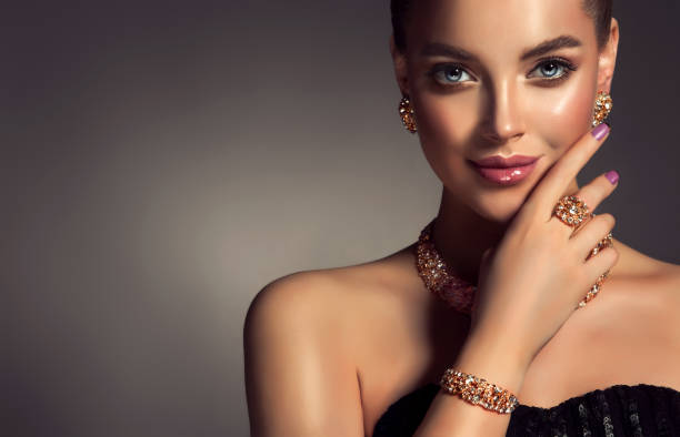 Magnificent lady in a perfect make up is shows jewelry set. Beauty portrait of young gorgeous woman is dressed in a jewelry set of necklace, ring and earings. Pretty  blue eyed model is demonstrating an attractive make up and manicure. gold bangles pics stock pictures, royalty-free photos & images