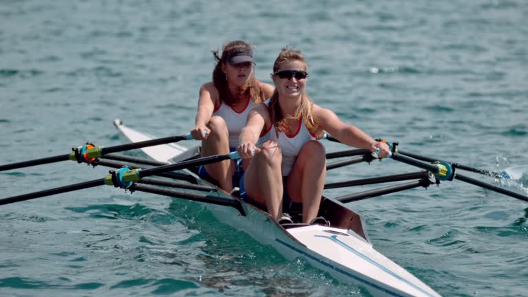 SLO MO Two female athletes sculling across the lake in sunshine