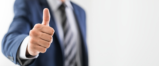Business man shows thumb up sign gesture. Isolated on grey background.