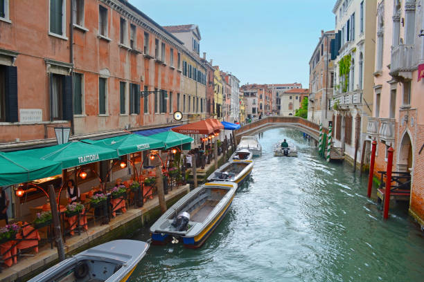 People eat at a waterside cafe along a canal in Venice Italy surrounded by buildings rich in history.