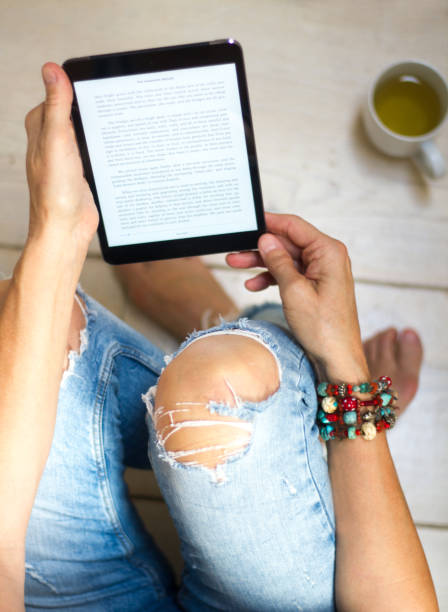 Woman in Distressed Jeans Relaxes with Tablet and Tea Woman in distressed jeans relaxes on a white wooden floor with a cup of tea and a digital tablet/e-reader (text is Mark Twain’s Innocents Abroad, public domain). hole in pants stock pictures, royalty-free photos & images