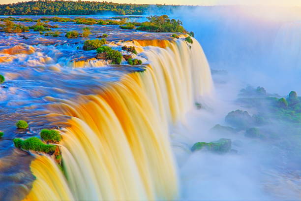 Impressive Iguacu falls, one of the most beautiful waterfalls in the world and one of the seven Wonders of Nature, blurred motion from long exposure at dramatic sunset - Idyllic Devil's Throat - international border of Brazilian Foz do Iguacu city, Parana State, Argentina Puerto Iguazu city, Misiones province and Paraguay - rainforest landscape panorama, South America caídas de iguazu impresionante paisaje, movimiento borrosa de la larga exposición al atardecer espectacular - garganta del diablo idílico - frontera internacional de brasil foz iguazu, parana, argentina puerto iguazu, misiones y paraguay - américa del sur