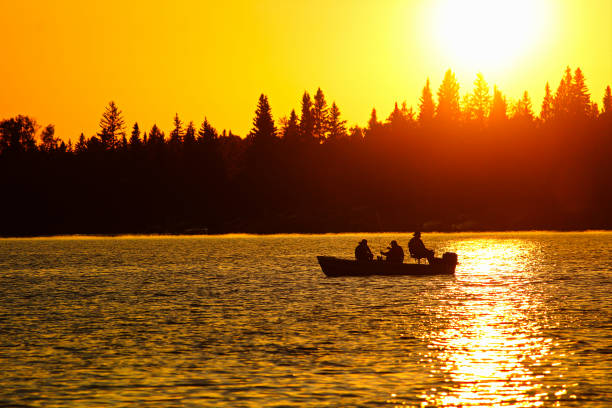 un bateau de pêche se découpant sur un ciel orange brillant - landscape canada north america freshwater fish photos et images de collection