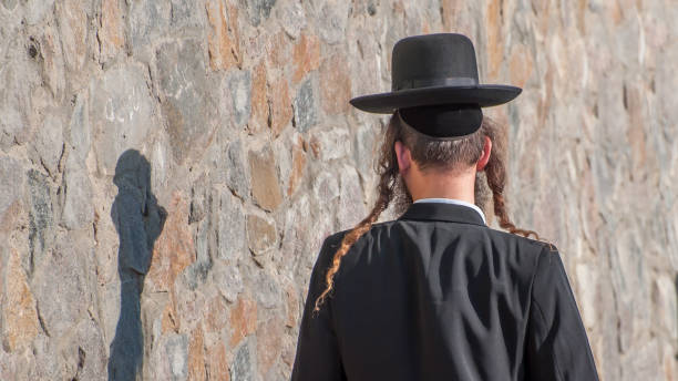 eine jüdische chassid in eine traditionelle ethnische hut mütze und mit langen payos auf dem hintergrund einer steinmauer. in der nähe von seinem schatten. - judaism jewish ethnicity hasidism rabbi stock-fotos und bilder